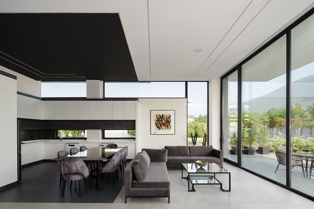 Modern open-plan kitchen and living room with sleek black and white decor, large windows.