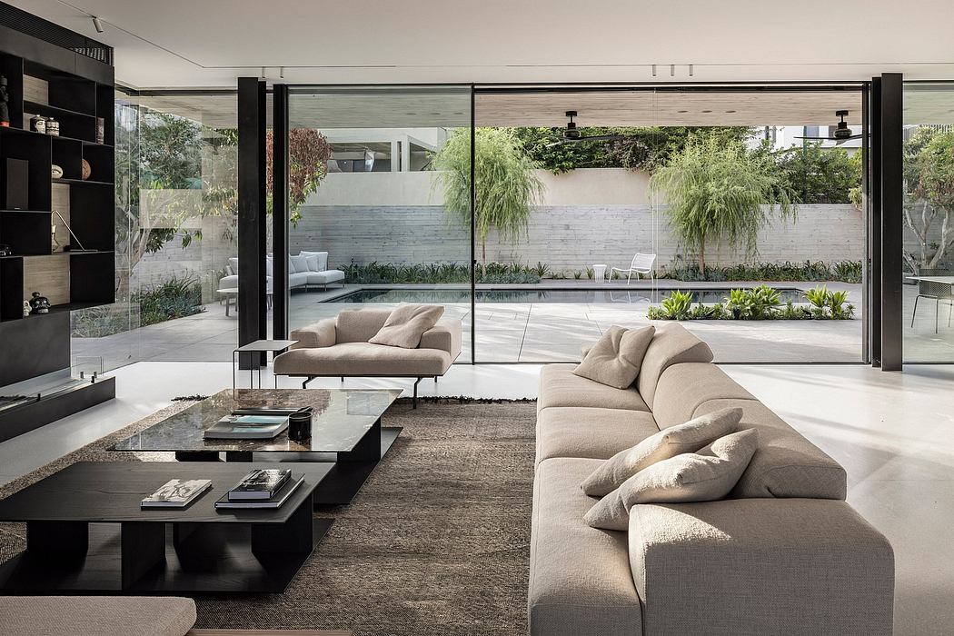 A modern living room with large glass walls overlooking a lush outdoor garden and pool.
