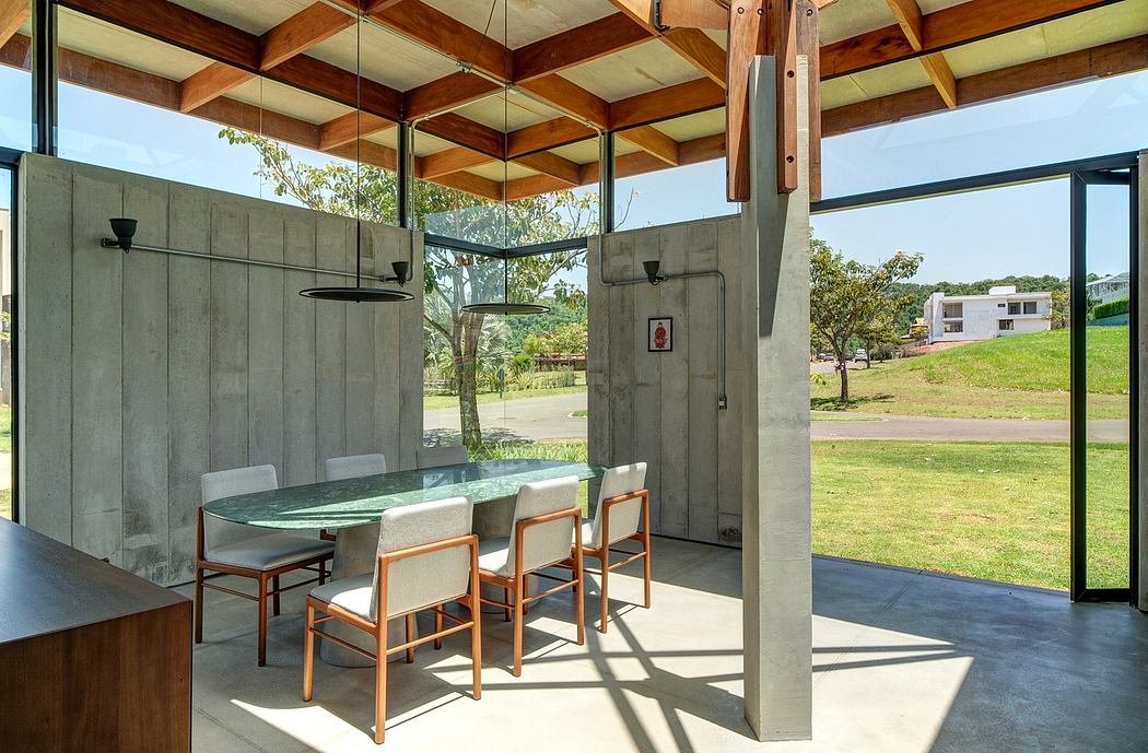 A modern, open-concept dining area with wooden ceiling beams, concrete walls, and glass panels offering scenic views.