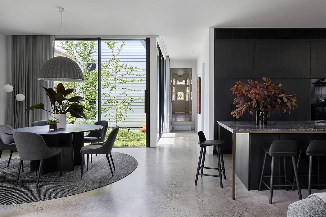 Sleek, modern dining space with black, minimalist furnishings and large windows overlooking greenery.