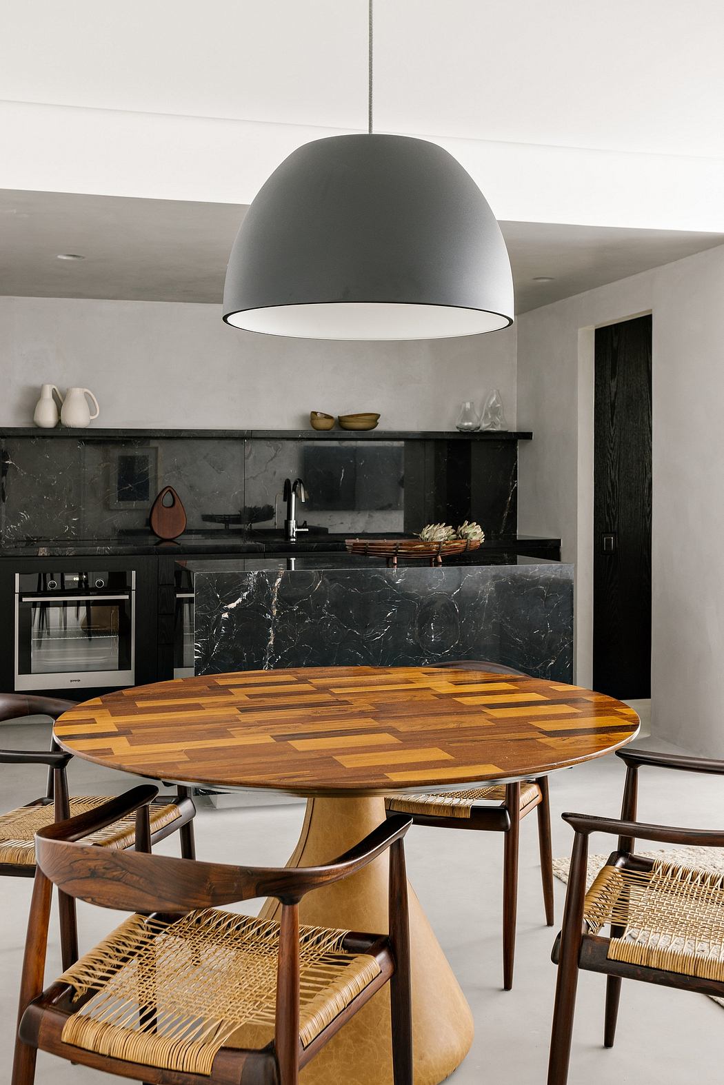 Sleek, modern kitchen with dark marble countertops, wooden dining table, and pendant light.