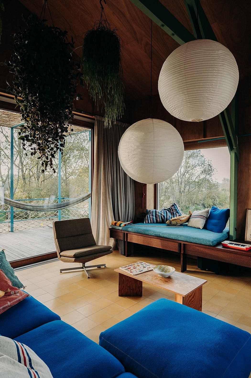 Cozy living space with wooden accents, pendant lamps, and a comfortable daybed overlooking nature.