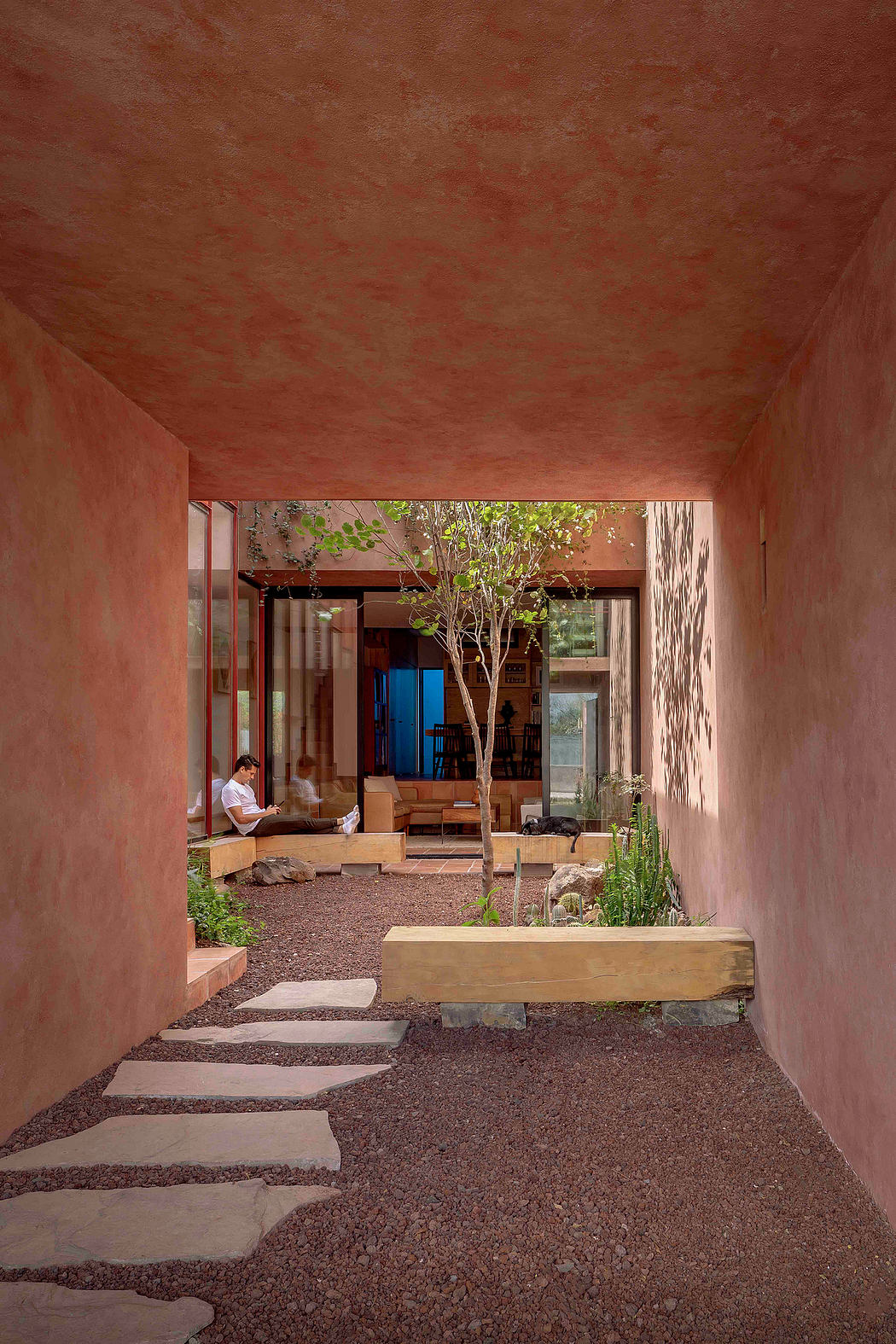 A warm, earthy-toned interior courtyard with a central tree and wooden seating.