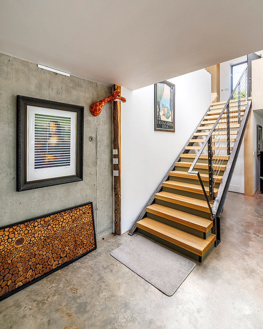 Sleek, modern staircase with wooden steps and metal railings. Concrete wall accented by framed artwork.