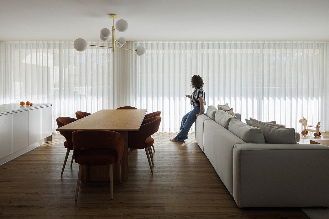 Modern, open-plan living room with mid-century furniture, floor-to-ceiling windows, and a decorative chandelier.
