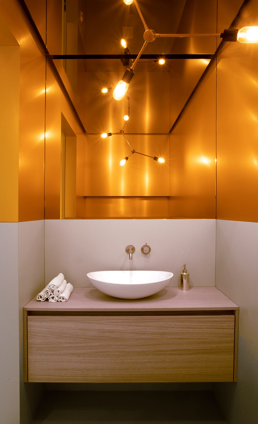 Warm, modern bathroom with a sleek white sink, wood vanity, and striking overhead lighting.