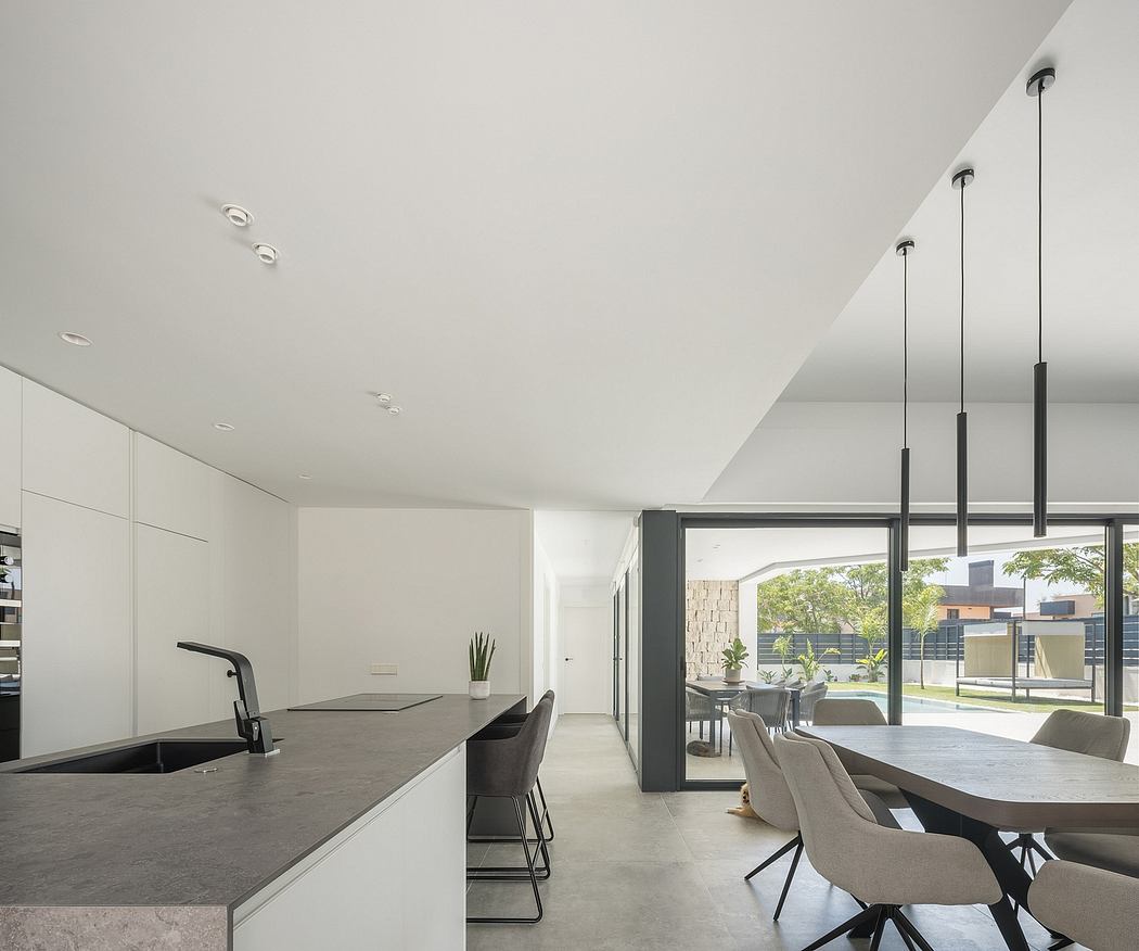 Minimalist open-concept kitchen and dining area with sleek furniture, large windows, and pendant lighting.