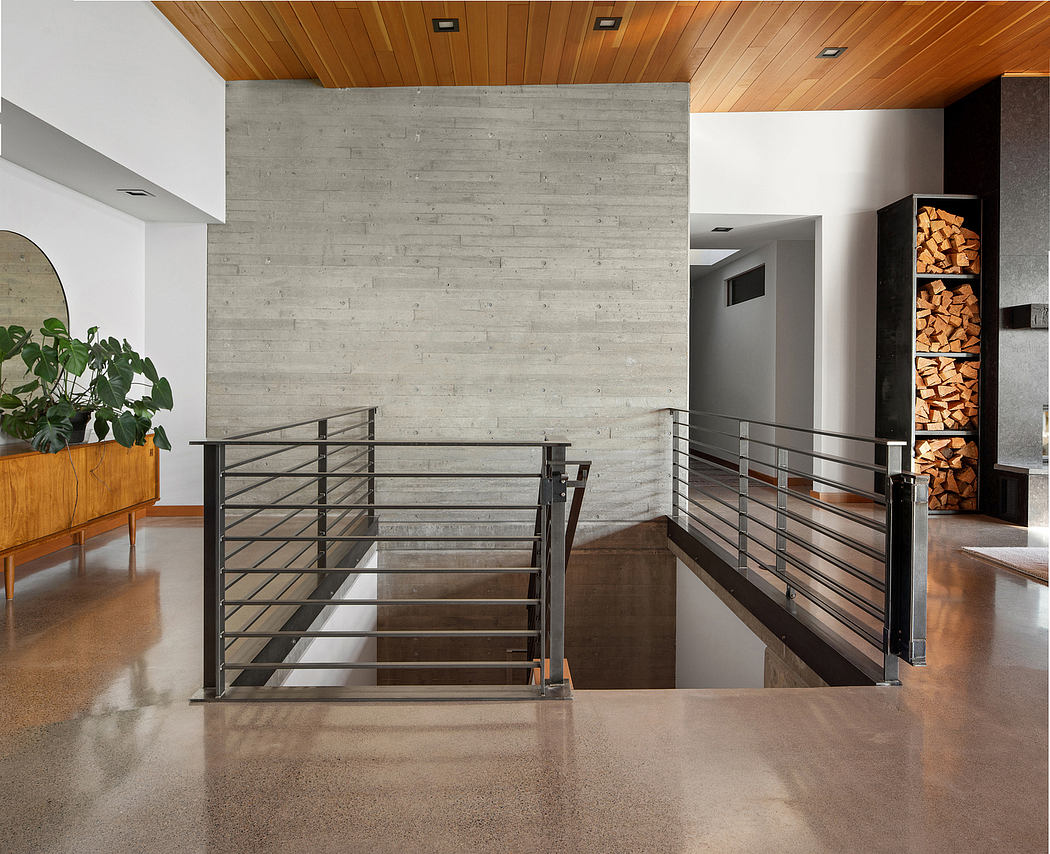Minimalist interior with concrete walls, wooden ceiling, and metal railings leading to a staircase.