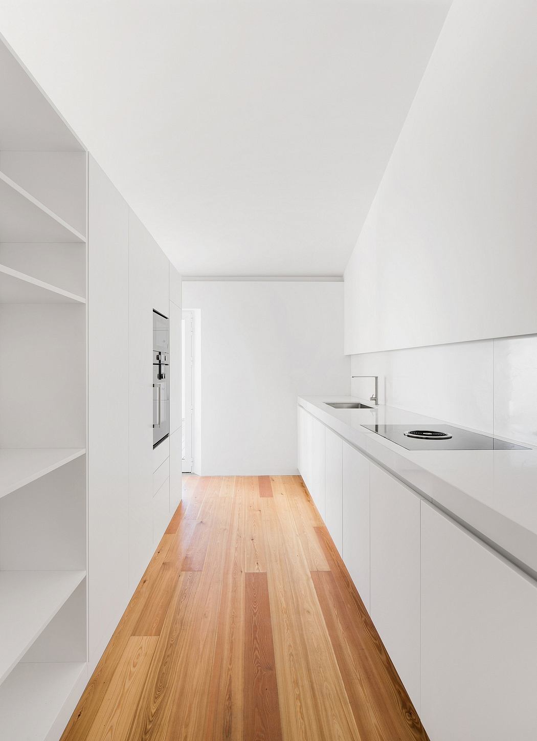 Minimalist kitchen with sleek white cabinets, wooden floors, and recessed lighting.