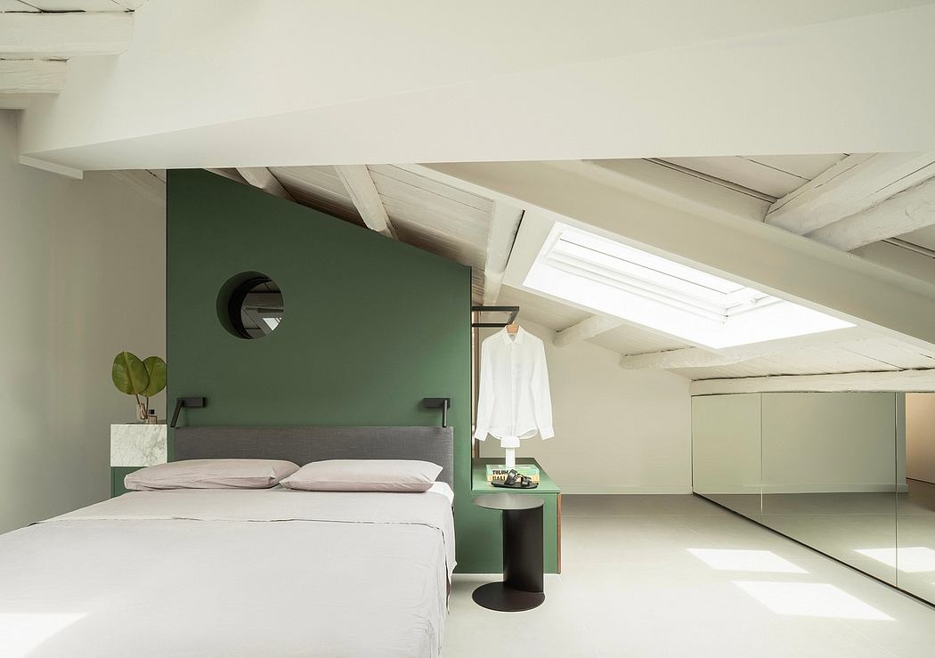 Minimalist and airy bedroom with green accent wall, slanted ceiling, and bright skylight.