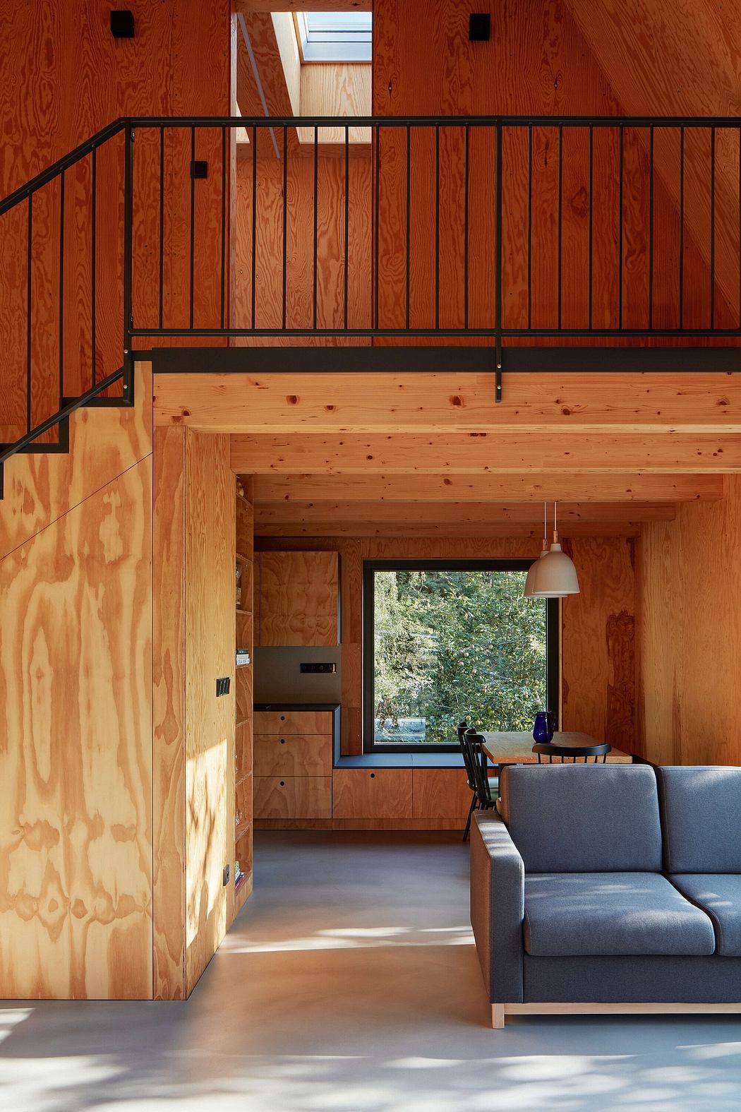 A cozy wooden cabin interior with a staircase, furniture, and a large window overlooking nature.