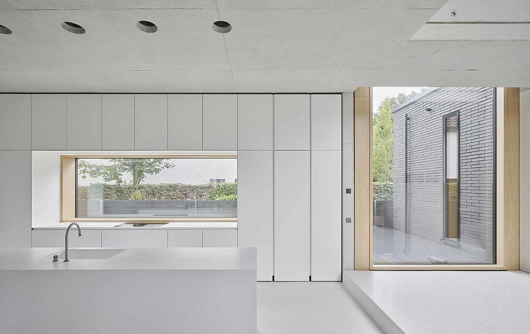 Modern minimalist kitchen with large window overlooking lush greenery and an adjacent open space.