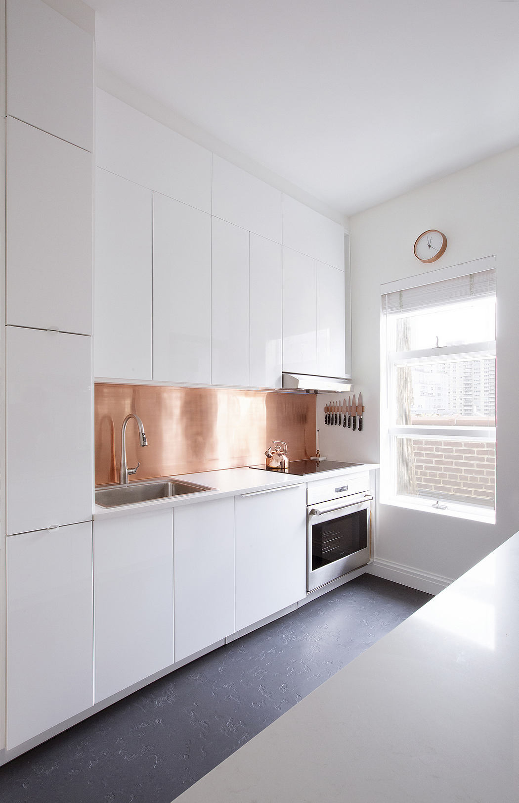 A modern, minimalist kitchen featuring white cabinetry and a copper backsplash.