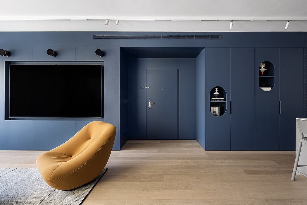 A modern, minimalist living space featuring a large TV, a yellow accent chair, and built-in storage.