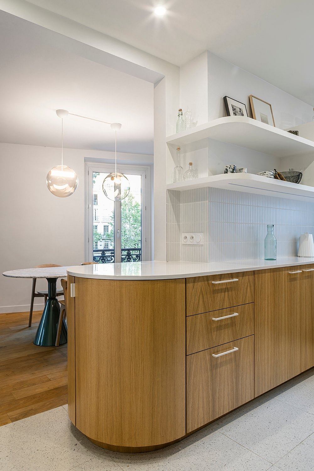 Modern kitchen with sleek wooden cabinets, open shelving, and a curved island with drawers.