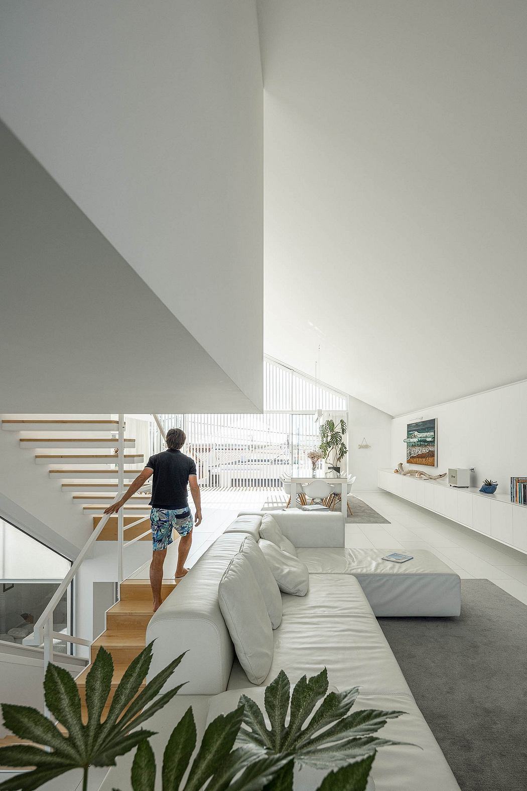 Airy, minimalist living room with sleek white furniture, wooden steps, and lush potted plants.