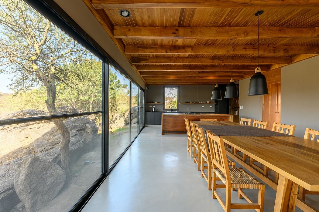 A modern cabin interior with a large window, wooden ceiling, and a long dining table.