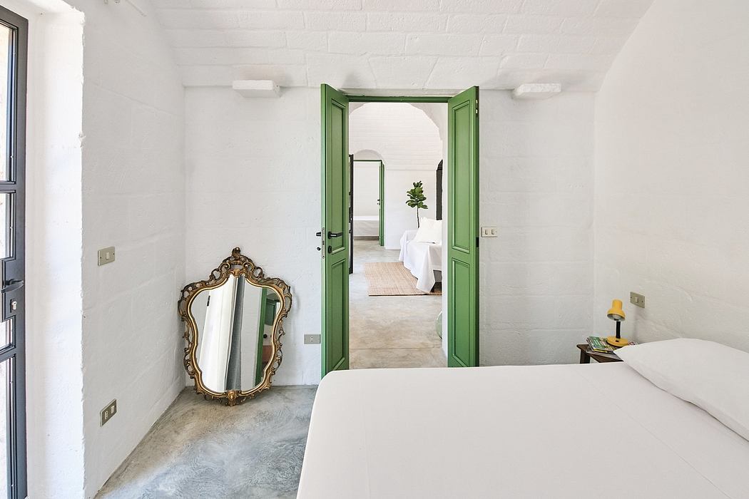 White minimalist bedroom with ornate gold-framed mirror and green double doors.