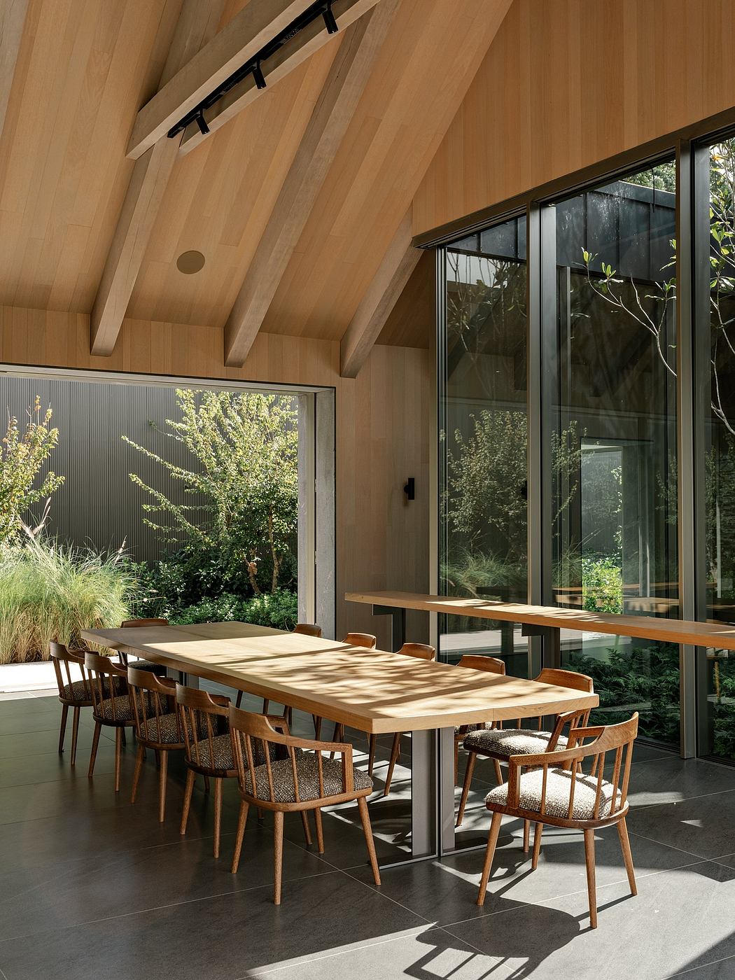 Spacious wooden-beamed interior with large windows overlooking lush greenery.