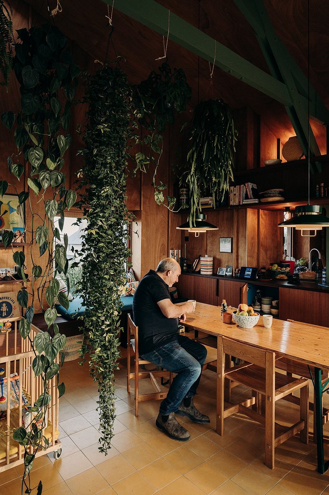 Cozy, plant-filled interior with wooden furniture, shelves, and a person sitting at the table.