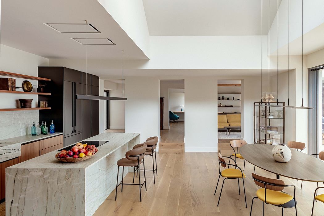 An open-concept modern kitchen and dining area with sleek cabinetry, natural wood flooring, and a marble island.