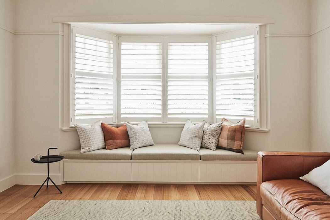 Cozy window seat with plush pillows, surrounded by large windows with white shutters.