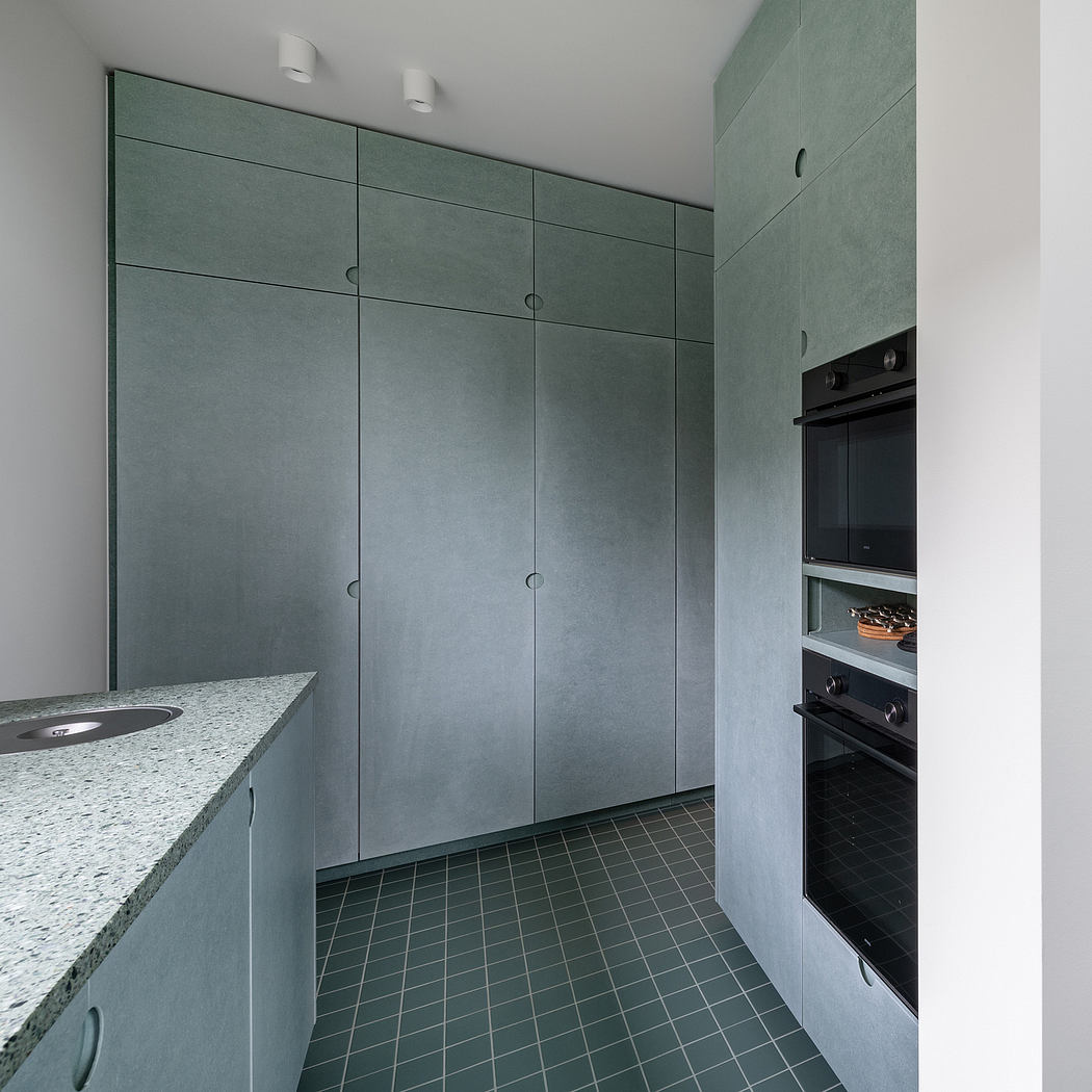Minimalist kitchen with monochromatic green cabinets, built-in appliances, and tiled floor.