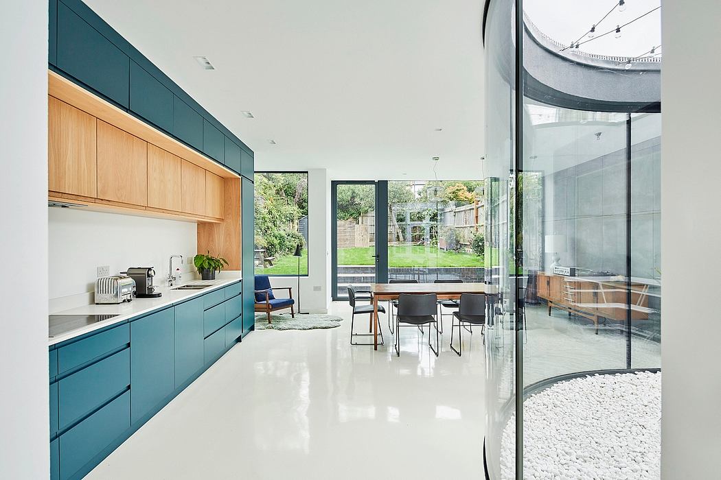 Modern open-plan kitchen with teal cabinets, glass walls, and garden view. Sleek, minimalist design.