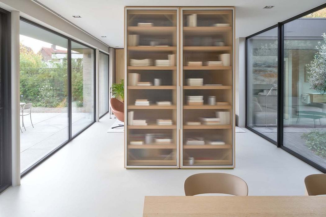 Minimalist open-plan living space with large glass doors, wooden shelving units, and neutral-colored furnishings.