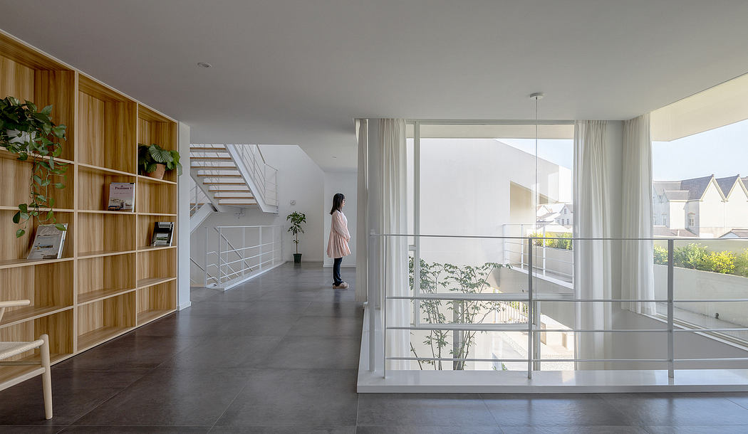 A modern, minimalist interior with a wooden bookshelf, glass walls, and a person standing.