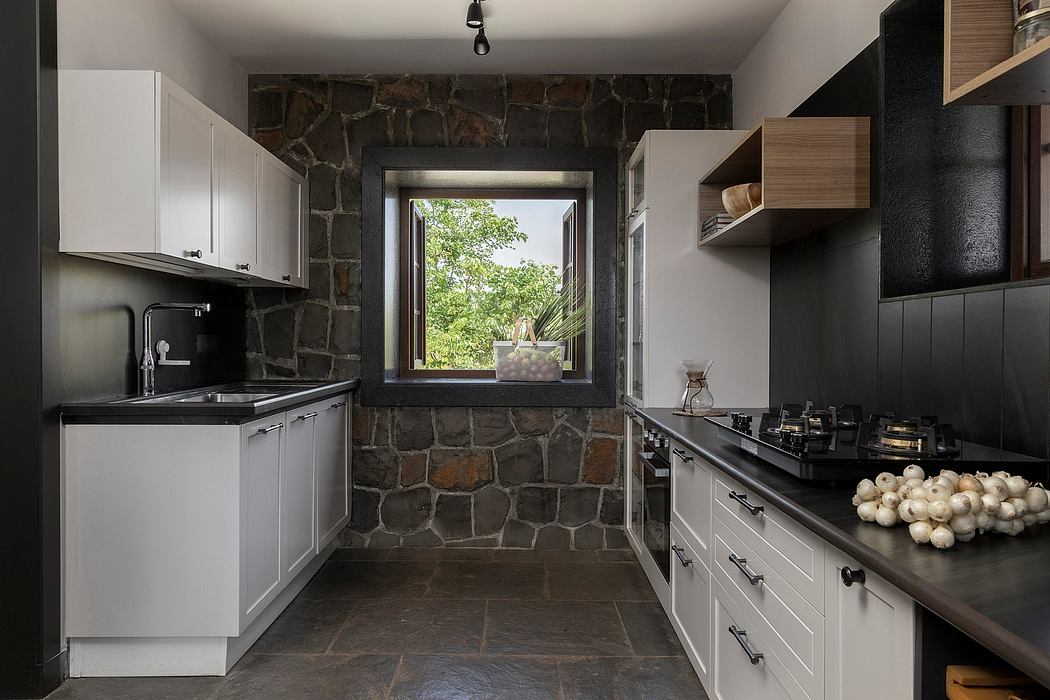 A rustic kitchen with stone walls, modern cabinets, and a window overlooking greenery.