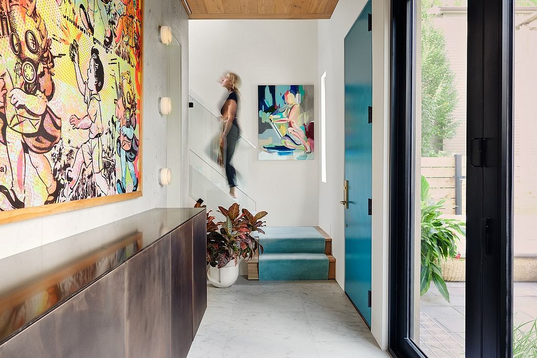 The image depicts a modern, colorful entryway with vibrant artwork, wood accents, and a glass door leading to a garden.