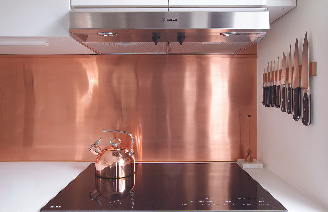 A modern kitchen with sleek copper backsplash, Bosch appliances, and a collection of knives.