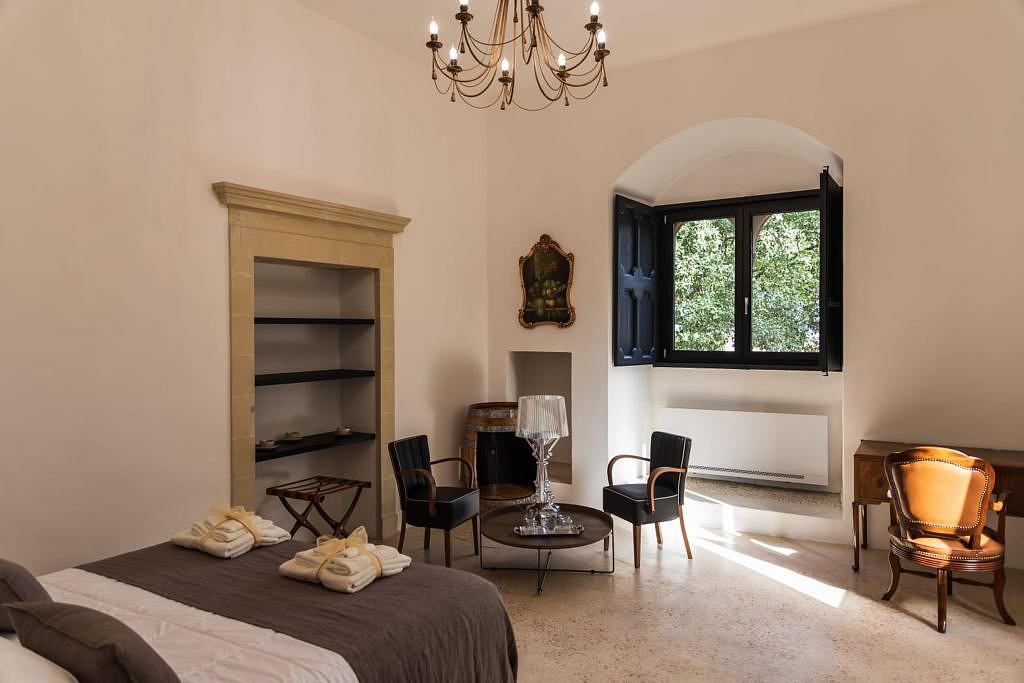 Elegant bedroom with ornate chandelier, shelves, and plush seating in a cozy setting.