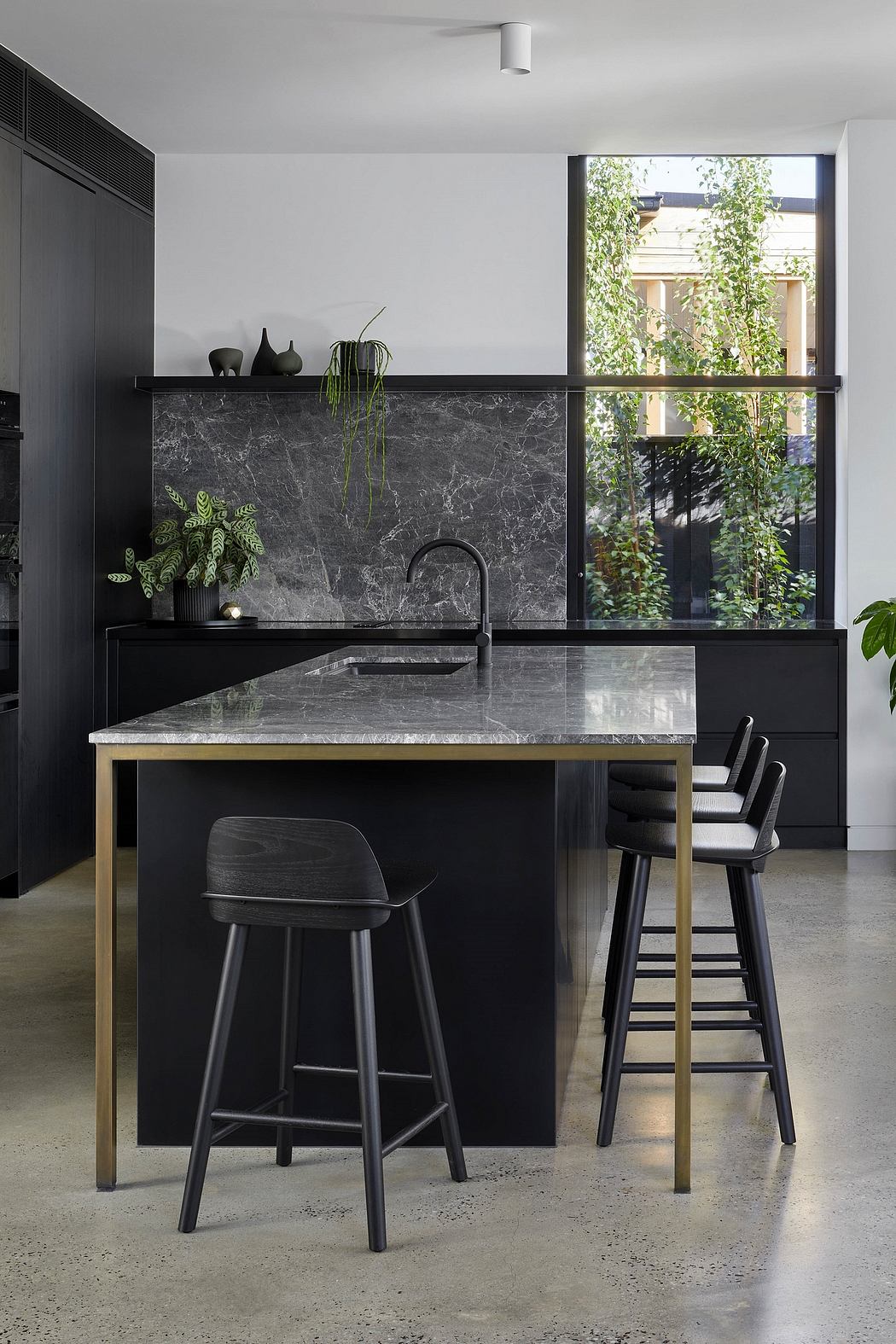 Sleek, modern kitchen with black cabinetry, marble countertops, and a large window overlooking greenery.