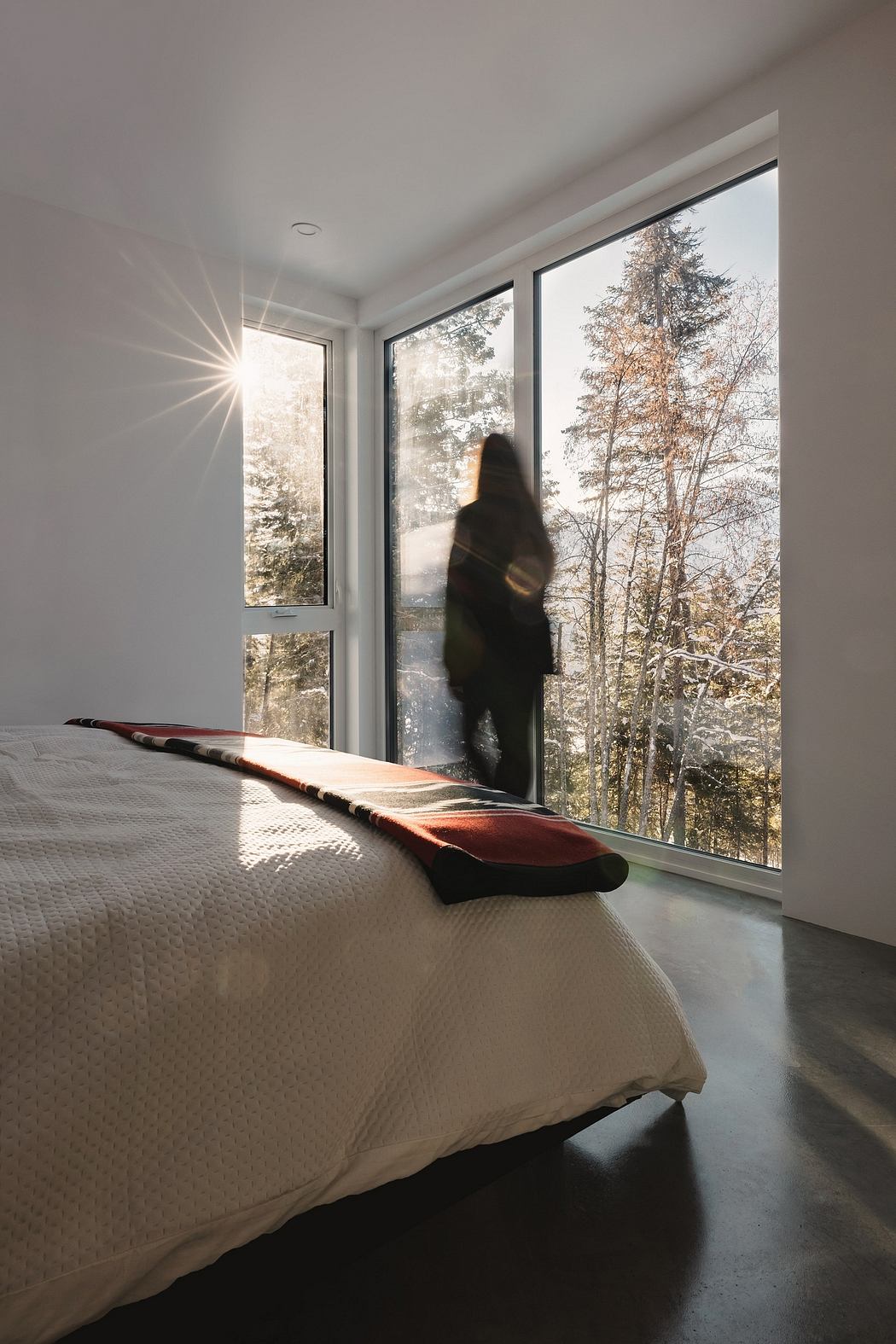 A modern bedroom with large windows overlooking a snowy forest landscape, showcasing an elegant design aesthetic.