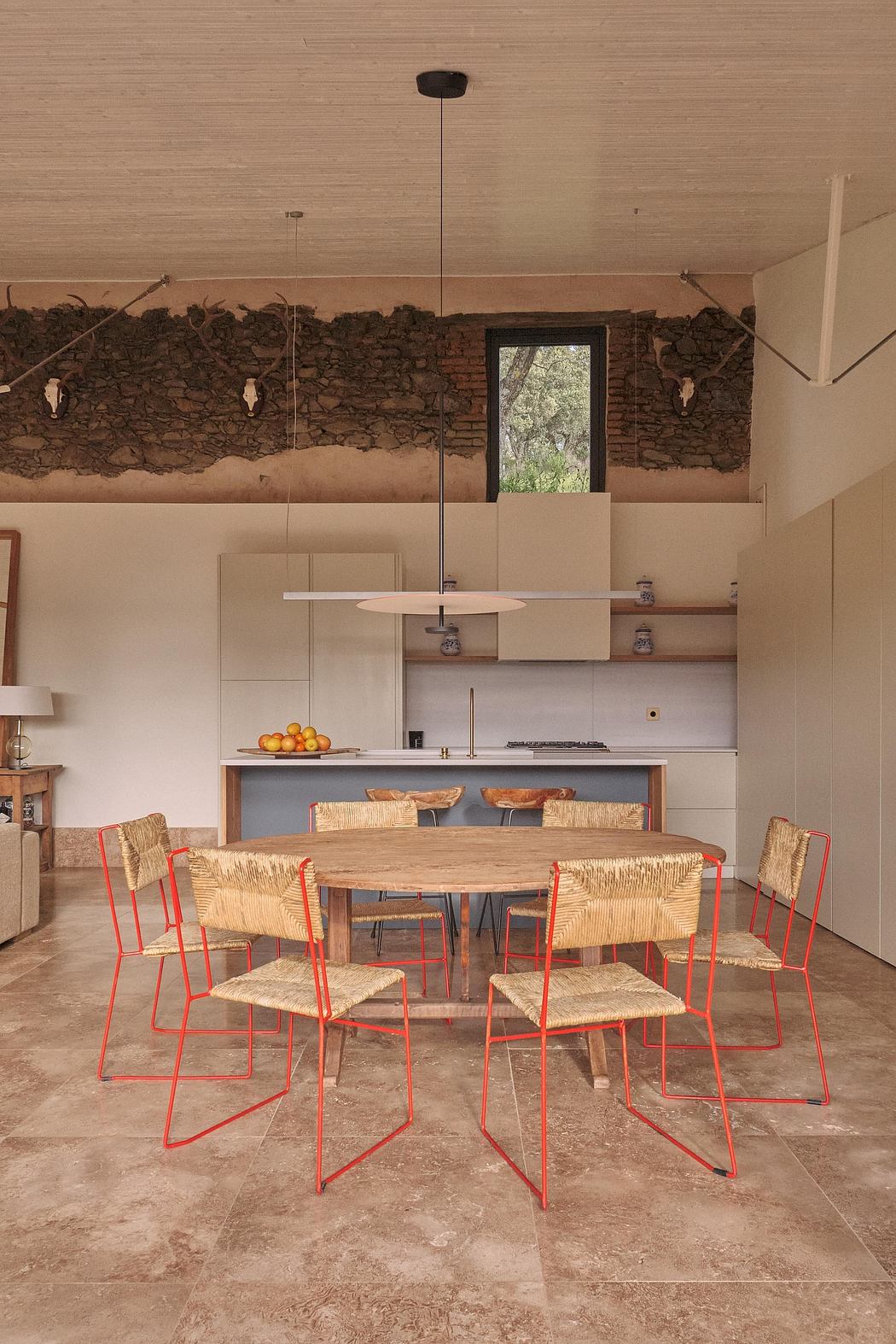 A cozy kitchen-dining area with exposed stone wall, wooden table, and vibrant red chairs.