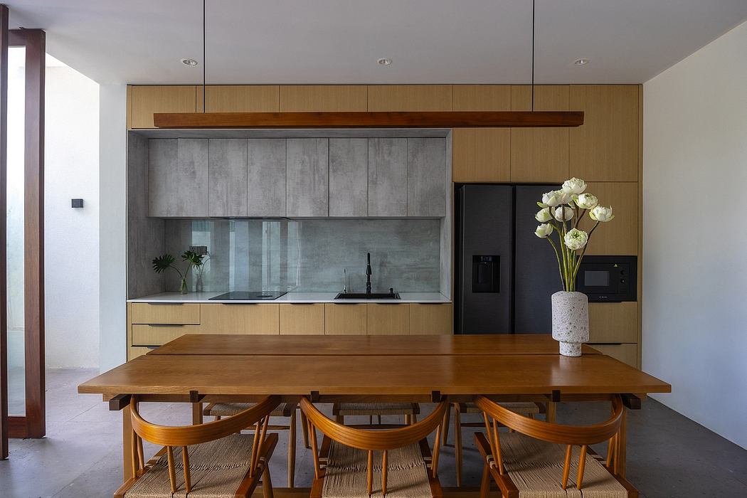 A modern kitchen with wooden cabinets, concrete backsplash, and a large dining table.