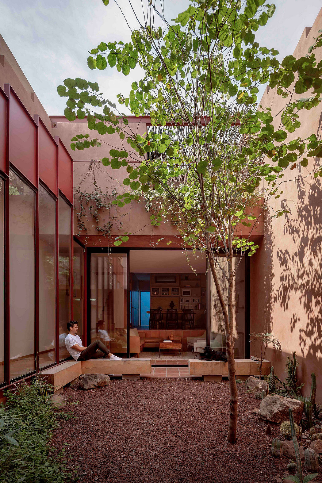 A contemporary courtyard design with a lush tree, red accents, and a cozy seating area.