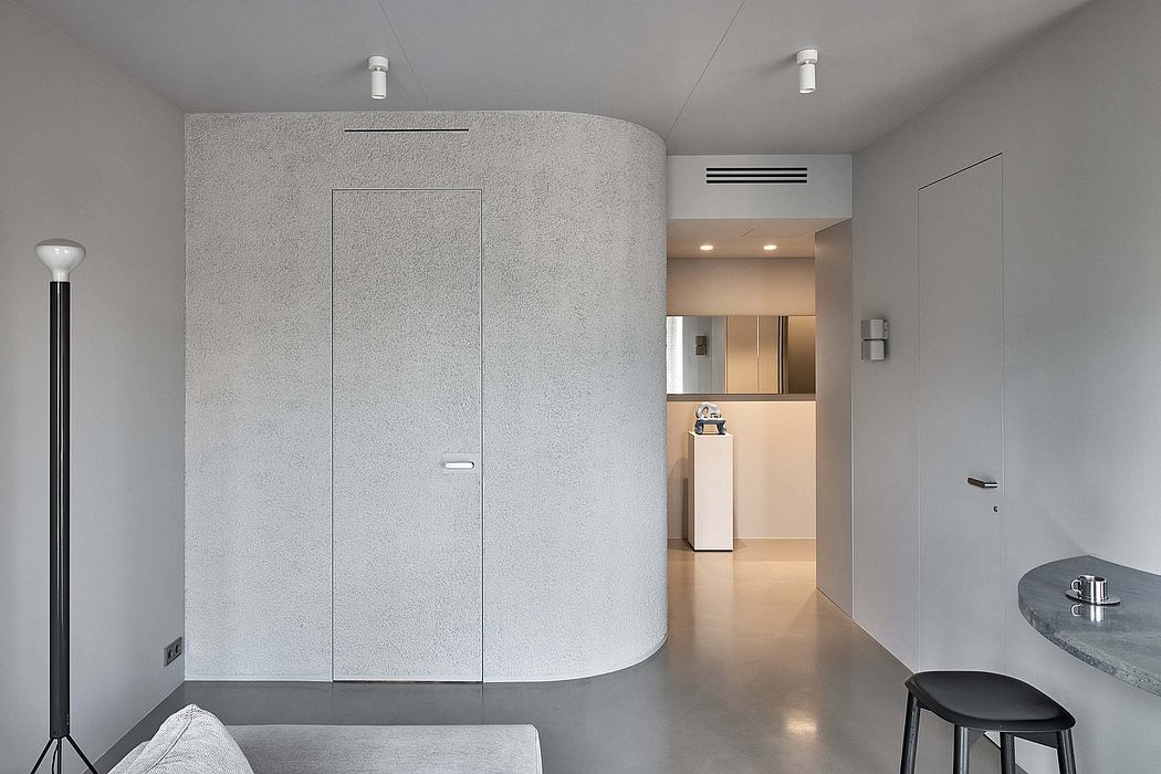 A minimalist, gray-toned interior with a curved wall, recessed lighting, and a marble table.