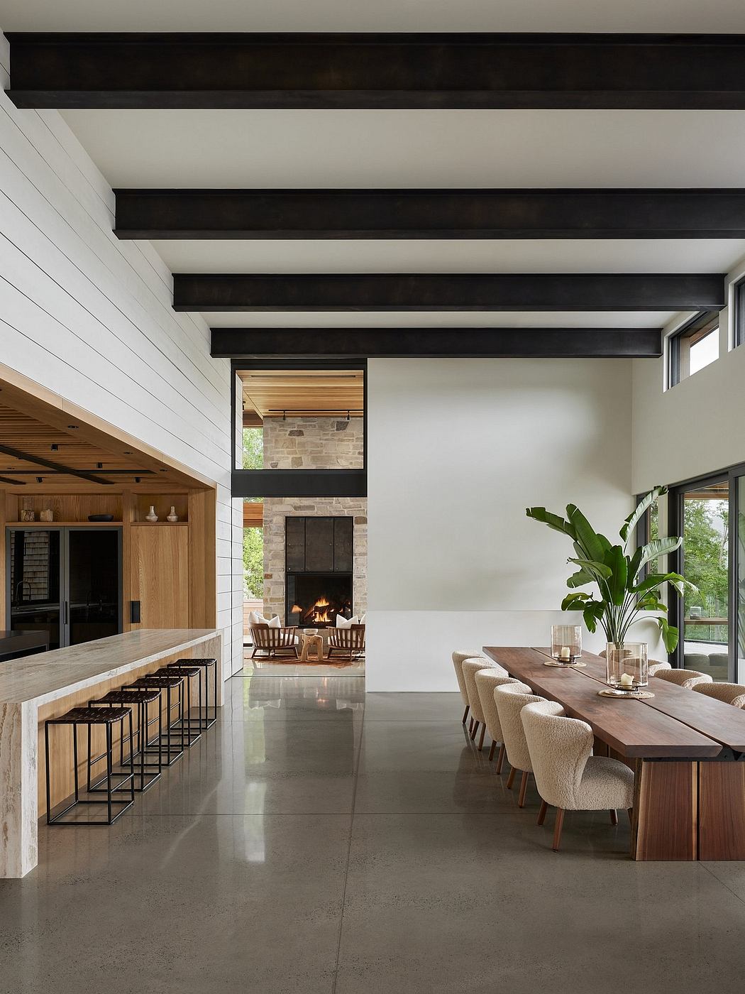 Sleek, modern interior with minimalist black beams, stone fireplace, and cozy dining area.