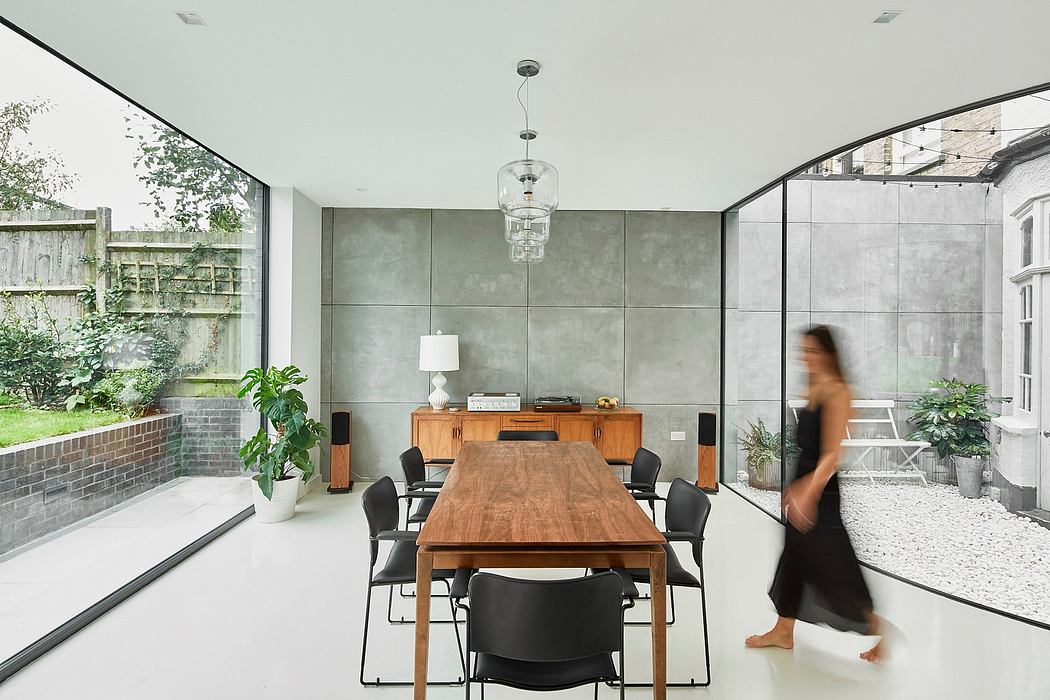Modern dining room with concrete walls, wooden table, and glass doors leading to a garden.