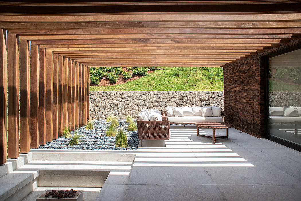Expansive covered patio with wood beams, stone wall, and minimalist outdoor furniture.