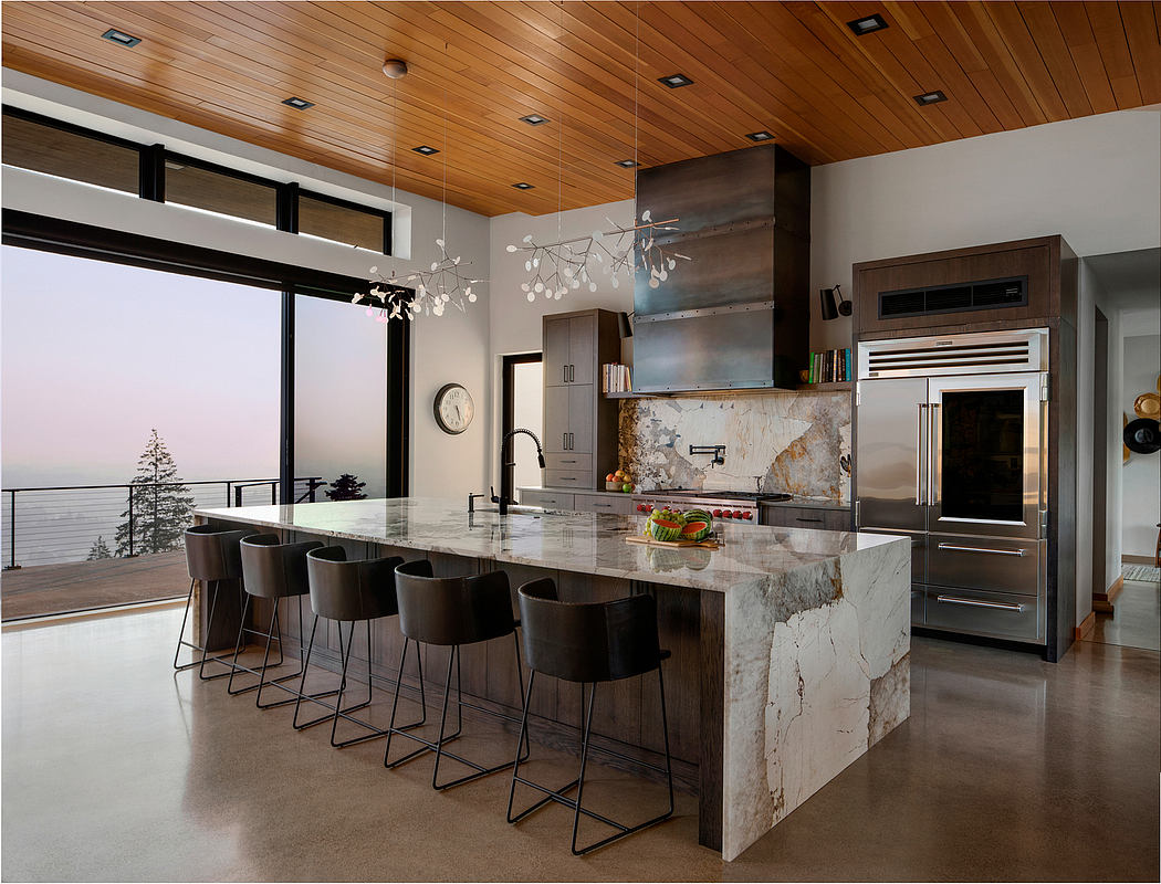 Spacious modern kitchen with sleek marble island, wood-paneled ceiling, and panoramic views.