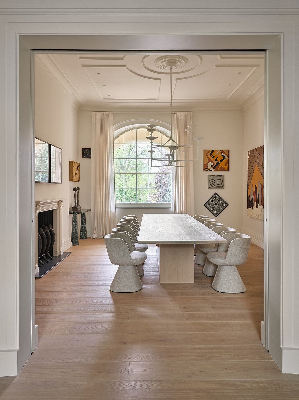 Opulent dining room with ornate ceiling, arched window, and eclectic artworks.