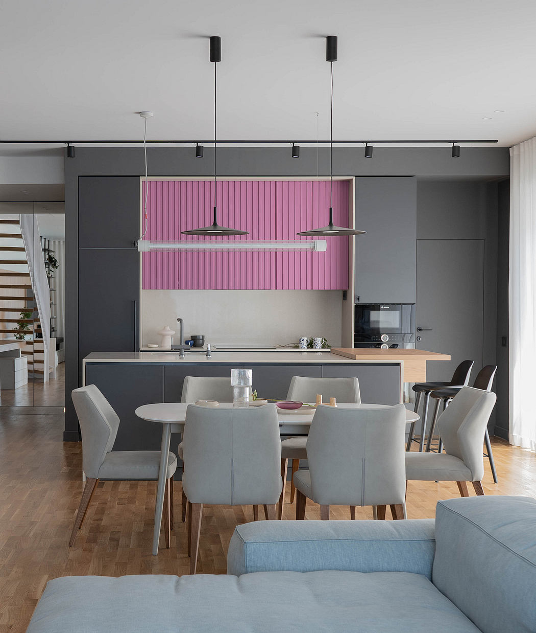 Sleek gray kitchen with pink accent wall, modern lighting, and gray dining furniture.
