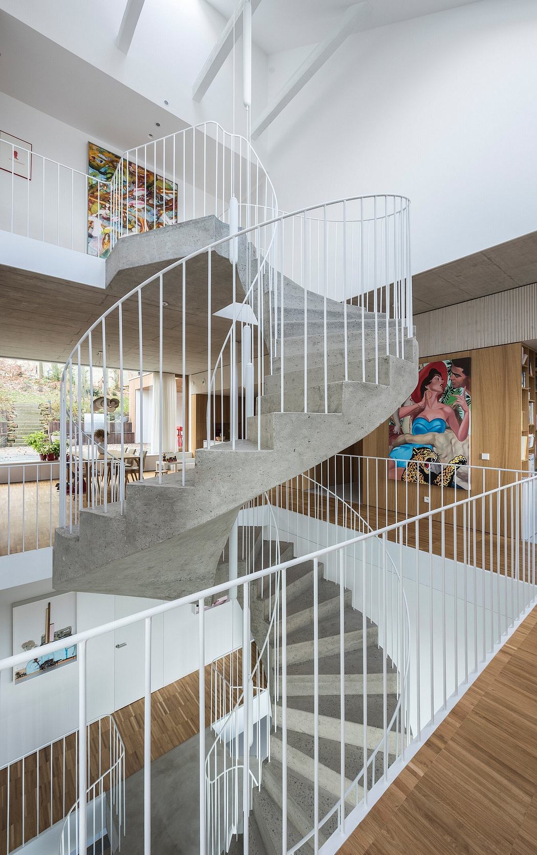 Striking spiral staircase with concrete treads and white metal railings, accented by colorful artwork.