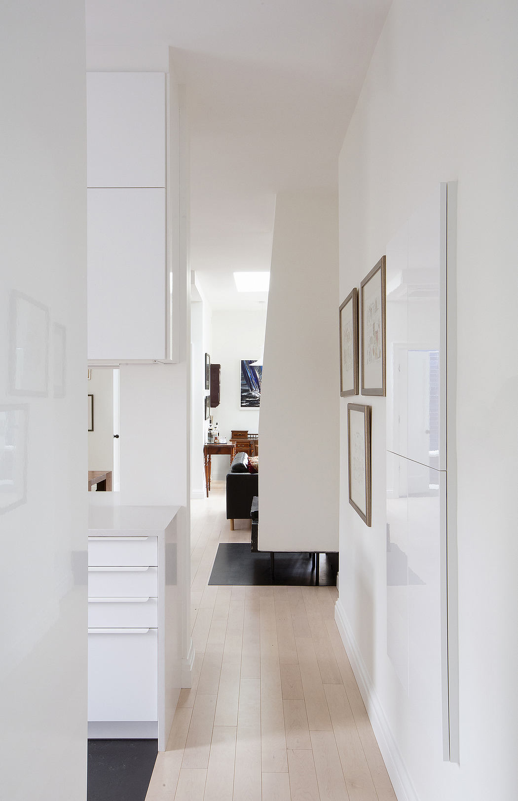 A minimalist, modern hallway with white walls, wooden floors, and framed artwork.