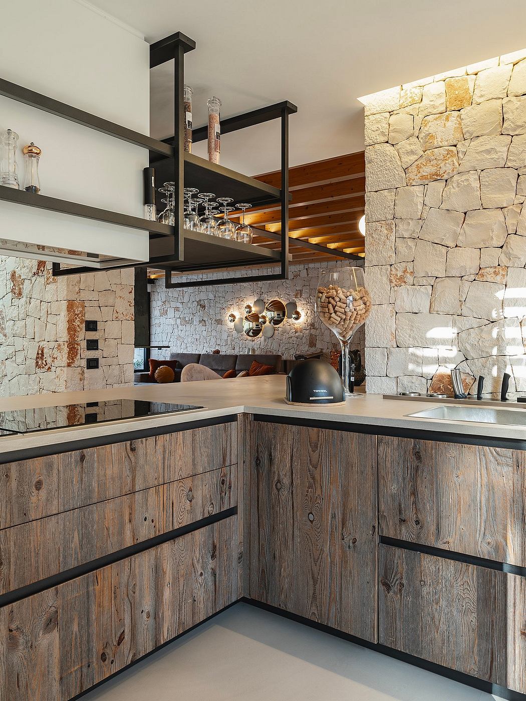 A cozy rustic kitchen with wooden cabinets, stone walls, and modern metal shelving.