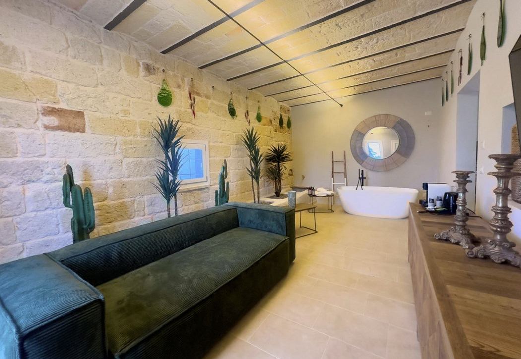 A spacious, rustic-style bathroom with exposed stone walls, a freestanding tub, and greenery.